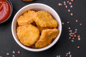 Delicious crispy chicken nuggets with salt and spices on a dark concrete background