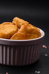 Delicious crispy chicken nuggets with salt and spices on a dark concrete background