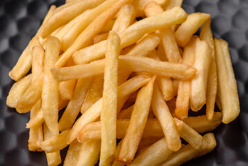 Delicious crispy french fries with salt and spices on a dark concrete background