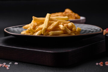 Delicious crispy french fries with salt and spices on a dark concrete background