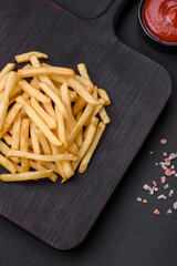 Obraz na płótnie Canvas Delicious crispy french fries with salt and spices on a dark concrete background