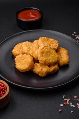 Delicious crispy chicken nuggets with salt and spices on a dark concrete background