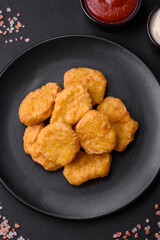 Delicious crispy chicken nuggets with salt and spices on a dark concrete background