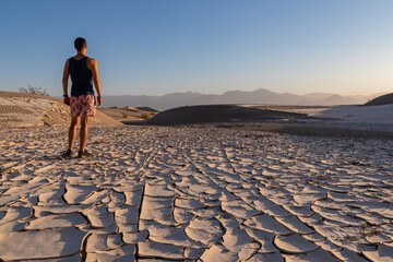 Man standing on dry cracked clay crust at Mesquite Flat Sand Dunes in Death Valley National Park, California, USA. Looking at pattern Mojave desert in summer with Amargosa Mountain Range in the back - Powered by Adobe
