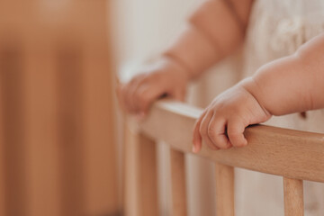 Mixed race toddler girl hands close up in round wooden baby crib at childrens room neutral tones