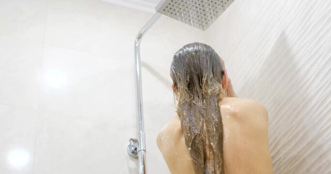A young woman refreshes her hair and body with a warm stream of shower, hair care