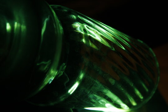 Vidrio de un vaso transparente refractado con luz verde incidente forma rayas y curvas con brillo, formando un dise&ntilde;o abstracto original sobre un fondo negro