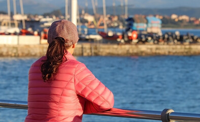 Woman in pink jacket looking at the horizon in a coastal landscape.