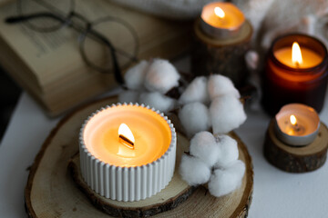 Cozy autumn or winter composition with aromatic candle, wool sweater, cotton, book. Aromatherapy, home atmosphere of cosiness and relax. Wooden background close up.