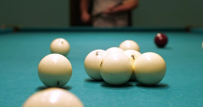 A man starts a game of billiards by breaking the balls with an accurate cue hit. The man takes aim and hits the pool cue ball. The concept of playing Russian billiards.