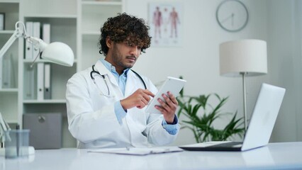 A doctor practitioner uses the digital tablet phone working while sitting in a modern office of a clinic or hospital Therapist healthcare worker typing browsing scrolling smartphone using app Indoor