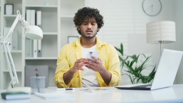 Unsuccessful payment internet scam Fraud victim Upset indian guy in office or home holds card and smartphone phone palm feels shocked, overspending money lost savings money stolen from bank problem