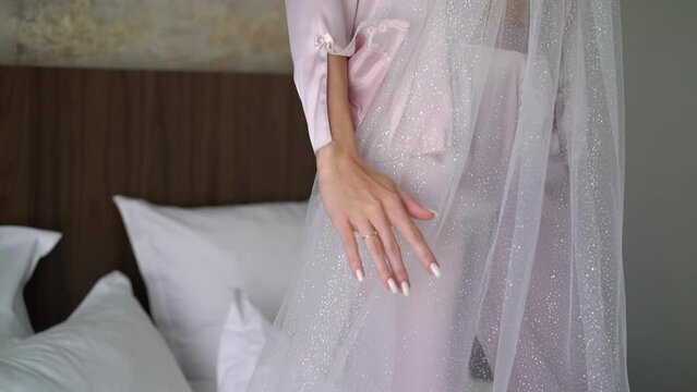 The bride in the morning in robe under her veil, spinning. Woman in underwear - white bra and pink robe in bedroom.