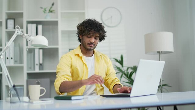 Young Indian man employee entrepreneur or freelancer working online typing browsing using laptop computer at workplace in office or home A programmer worker agent or coder has a busy job note notepad