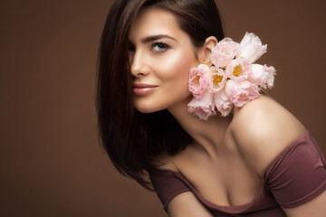 Beauty Girl with natural Makeup and Pink Flowers Bouquet over Brown Background. Woman Face Skin Care and Spa Cosmetology. Fashion Model Portrait with Spring Tulips