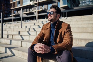 Handsome man with sunglasses enjoying sunny winter or spring day in the city sitting on stairs