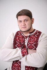 adult handsome man in a white embroidered shirt with large red embroidery looks intently into frame he crossed arms