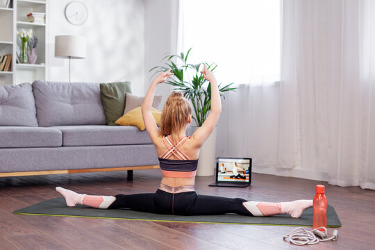 Child Girl In Sportswear Watching Online Video On Laptop And Doing Fitness Exercises At Home.