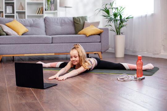 Child Girl In Sportswear Watching Online Video On Laptop And Doing Fitness Exercises At Home.