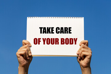 Take care of your body text on notebook paper held by 2 hands with isolated blue sky background. This message can be used as business concept about taking care of your health.