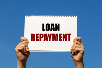 Loan repayment text on notebook paper held by 2 hands with isolated blue sky background. This...