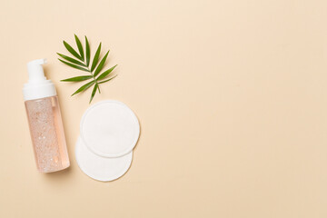 Foaming facial cleanser and with eco pads on color background, top view
