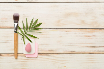 Make up brush and sponge on wooden background, top view