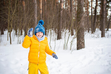 Fototapeta na wymiar happy smiling child in a jacket, hat, scarf, walks in a winter sunny forest on a snowy day
