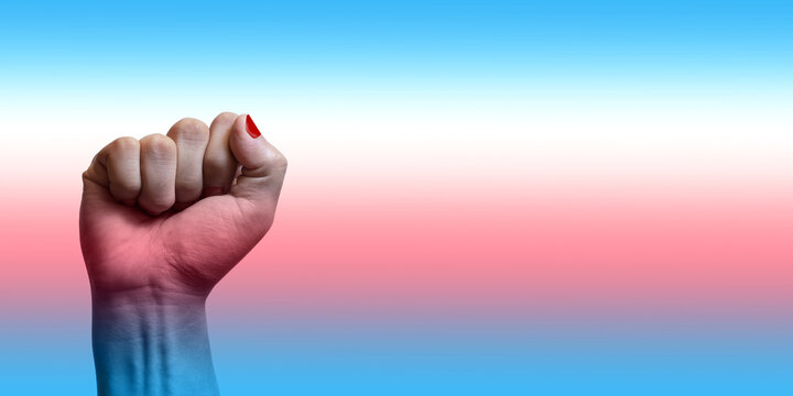 Pu&ntilde;o en alto de una persona joven en fondo degradado y colores de bandera transg&eacute;nero; orgullo transg&eacute;nero.