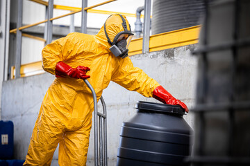 Worker in protective hazmat suit, gas mask, gloves moving barrels with aggressive chemicals on forklift inside factory. © littlewolf1989