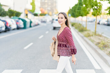 Side view of young trendy ethnic female with makeup and cigarette walking on road in city while looking at camera