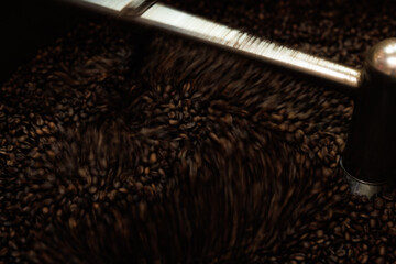 Close-up and low speed shutter blurred to capture the movement of dark roast coffee bean moving in rotating mixing coffee roaster spin machine process.