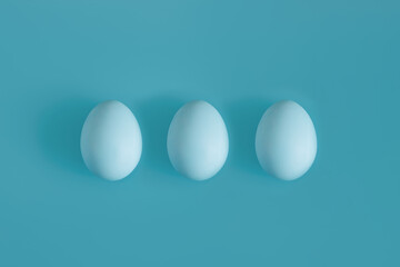 Three white egg on a light blue background in the center. Background concept for design, visual art, minimalism, easter.
