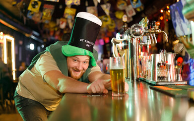 red-haired guy in a leprechaun mask for st. patrick's day takes a beer