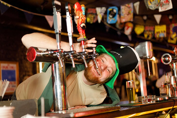 ginger guy tries to drink beer from the faucet behind the bar