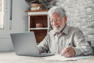 Aged remote worker. Concentrated senior male in glasses work on laptop from home office read email electronic document. Old age man employee freelancer sit at kitchen table by pc typing report online. - obrazy, fototapety, plakaty