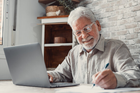 Aged remote worker. Concentrated senior male in glasses work on laptop from home office read email electronic document. Old age man employee freelancer sit at kitchen table by pc typing report online.