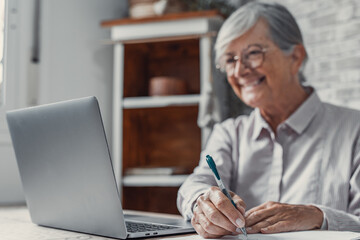 Aged remote worker. Concentrated senior female in glasses work on laptop from home office read...
