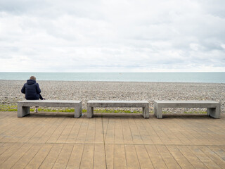 A woman sits on a bench alone with her back to the camera. Coast of the sea. Cloudy at the resort.