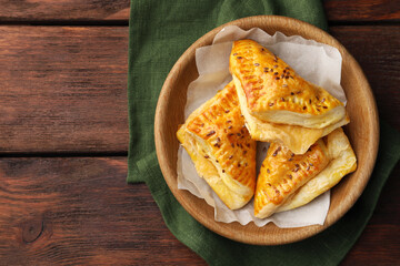 Fresh delicious puff pastry with cheese in bowl on wooden table, top view. Space for text
