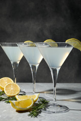 Martini glasses of refreshing cocktail decorated with lemon slices and rosemary on light grey textured table