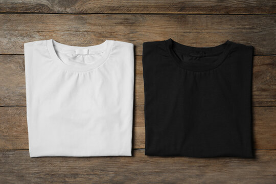 Stylish white and black T-shirts on wooden table, flat lay