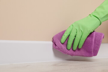 Woman in protective glove cleaning plinth with washcloth indoors, closeup. Space for text