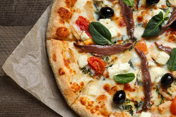 Tasty pizza with anchovies, basil and olives on wooden table, top view