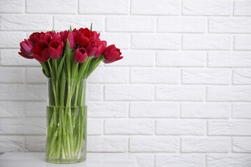 Bouquet of beautiful tulips in glass vase on white table indoors. Space for text