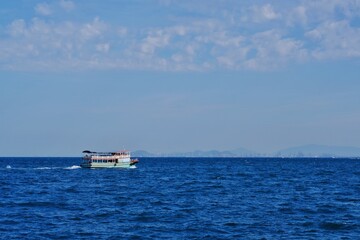 Passenger boat crossing to the island against the blue sea ocean against bright sky.