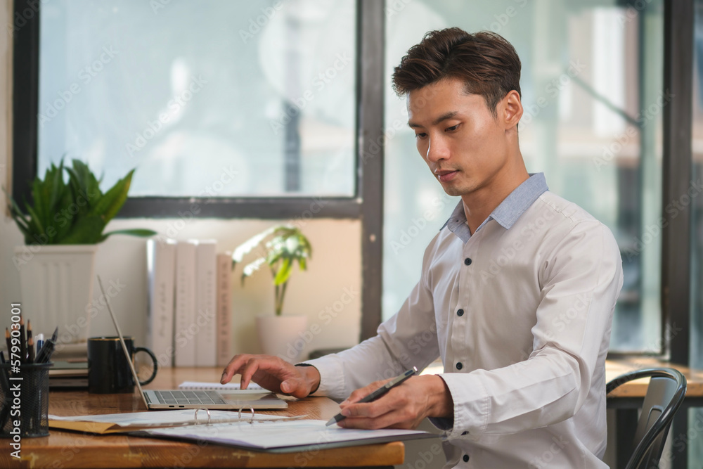 Poster start up businessman writing new idea on notepad and using laptop in bright modern office..