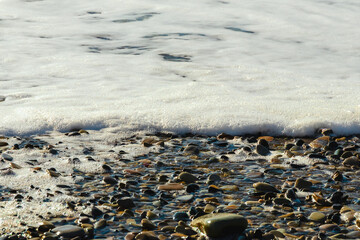 A soft sea wave on a sandy beach. White foam of the coastal wave on the sandy shore. Close-up of a wave on the Black Sea coast. Coastal waves. Selective focus. View of the waves of the Black Sea.