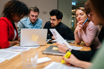 Portrait of multiethnic businesspeople talking working on laptop, discuss business project sitting at table in office. Diverse colleagues or partners brainstorm on computer at meeting.