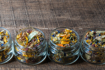 Dry flower and herbal tea leaves in a glass jar on wooden background. Herbal collection of...